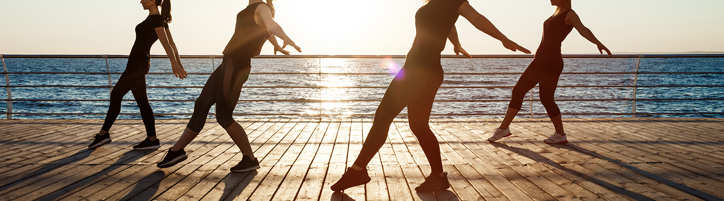 Silhouettes of sportive women dancing near sea at sunrise